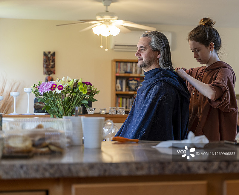 自己动手 - 家庭理发。一个十几岁的女儿给她的父亲，一个50岁留长发的中年男人理发。图片素材