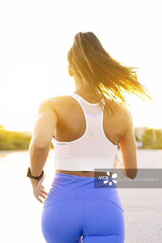 在晴天，在城市中对着蓝天在道路上跑步的女人图片素材