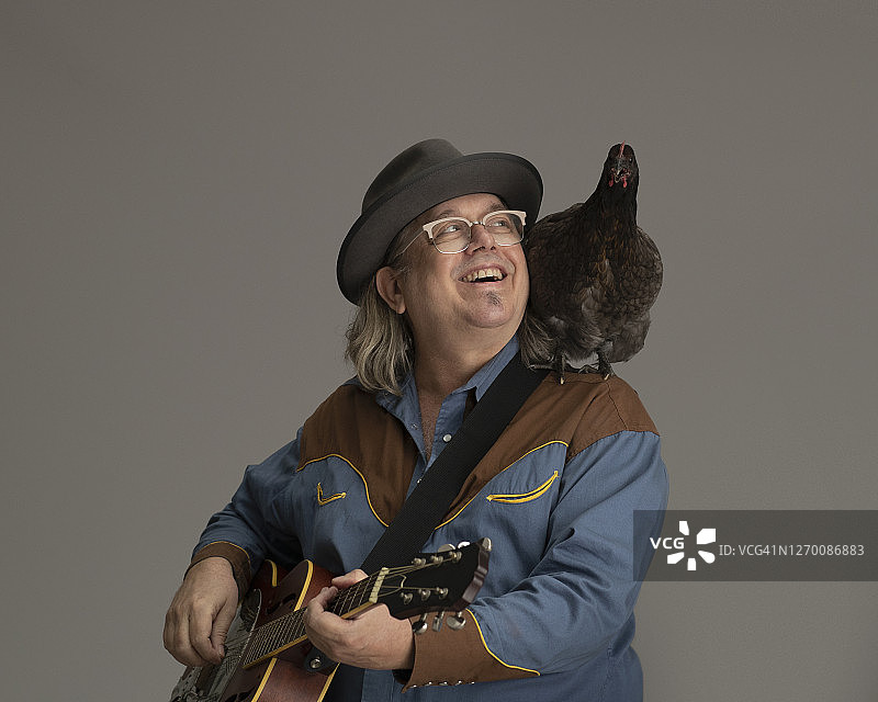 吉他手肩扛小鸡坐在凳子上的人物肖像图片素材