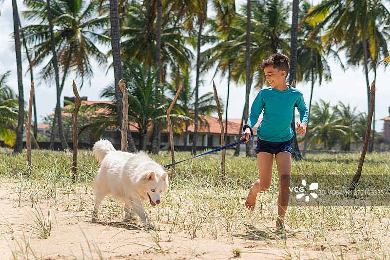 男孩在沙滩上和白狗一起奔跑图片素材