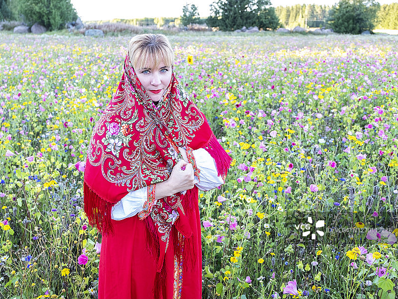年轻的白人女性，身穿俄罗斯和乌克兰传统民族服装，头戴红色连衣裙和披肩，背景是野花草地，肖像图片素材