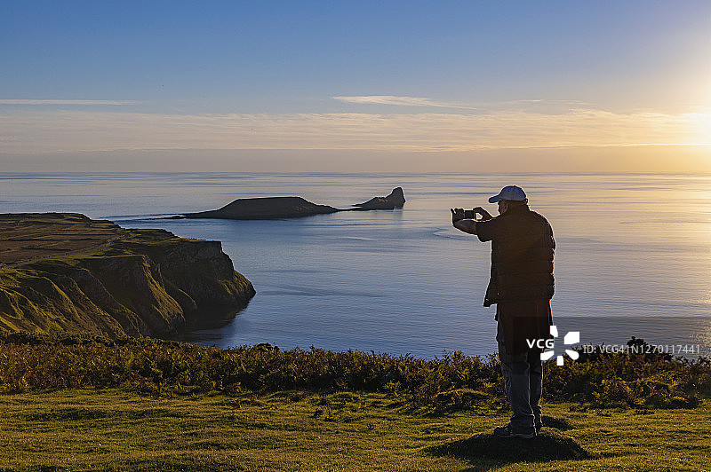 罗西里湾日落：一位年长的男人用智能手机拍照图片素材