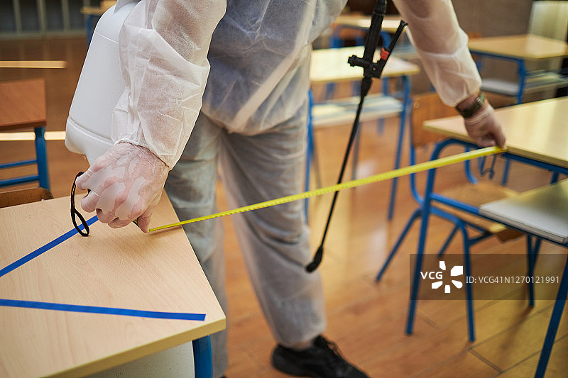 疫情期间身穿防护服戴着外科手套的男人测量学校课桌之间的距离图片素材