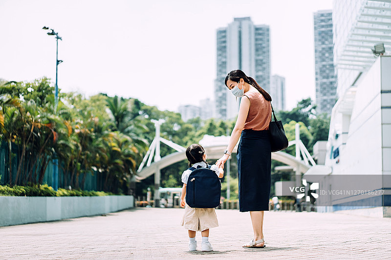 可爱的亚洲女学生牵着她母亲的手，两人都戴着防护口罩，在新冠疫情期间去上学。图片素材
