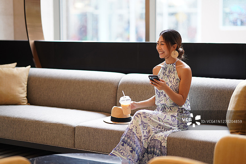 亚洲女游客在酒店大堂沙发上手持咖啡使用手机图片素材