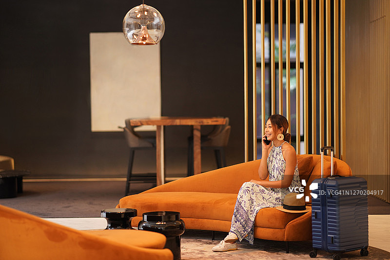 在酒店大堂沙发上使用手机微笑交谈的旅行女性的奢华生活方式图片素材