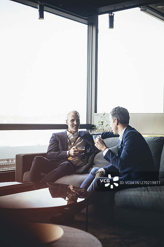 微笑的商人与同事在办公室喝茶讨论图片素材