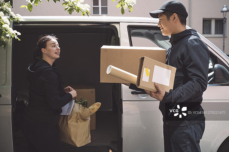 送货员与微笑的同事交谈，同时在卡车附近拿着包裹图片素材