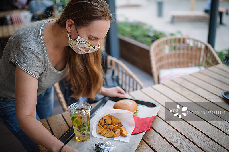 在咖啡馆或餐厅的开放式露台上戴着防护口罩端着食物的女人图片素材