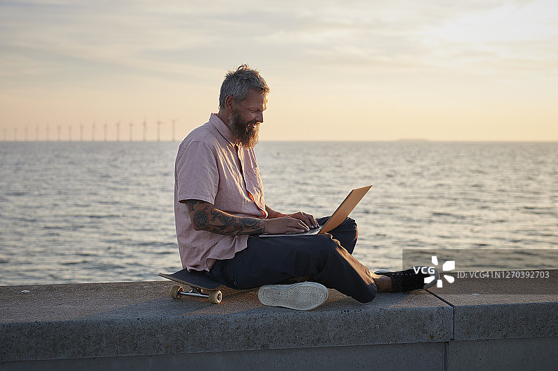 潮人坐在滑板上使用笔记本电脑图片素材