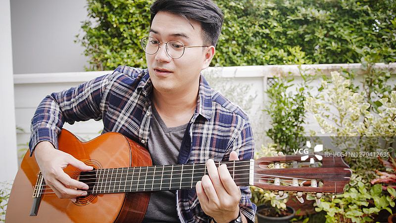 亚洲男人在家里的户外花园用平板电脑进行吉他视频通话图片素材