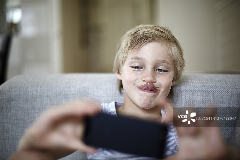 在家玩手机吐舌头的男孩图片素材