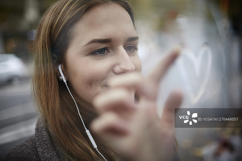 戴着耳机在玻璃上画爱心的年轻女子图片素材