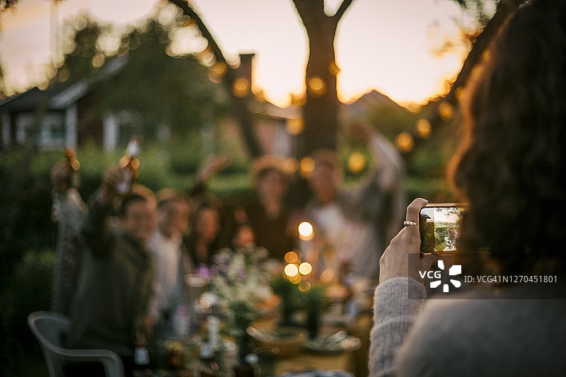 在院子里聚餐时为朋友拍照的女人图片素材