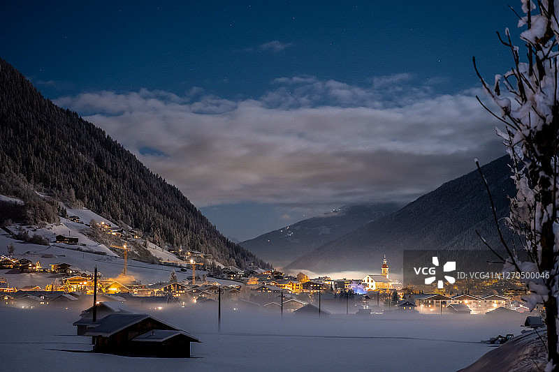 冬季夜景：俯瞰奥地利蒂罗尔州新施蒂夫特市和教堂，背景是山脉和云彩。山谷里有雾的寒冷夜晚图片素材