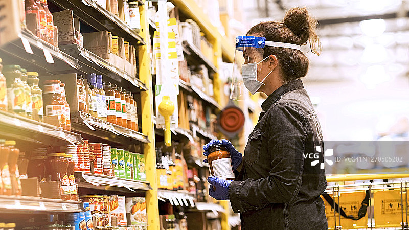 中年妇女在超市过道购买食品，戴防护口罩、外科手套和面罩图片素材