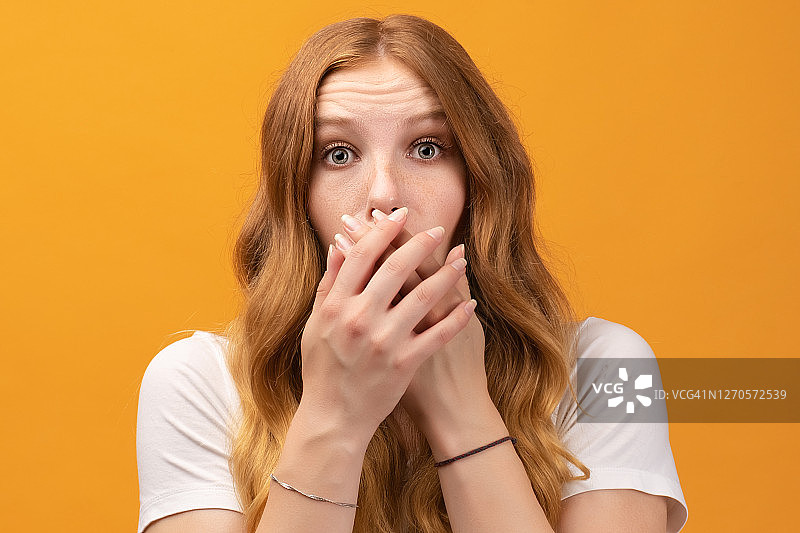 穿着白色T恤的红发波浪卷受惊女孩肖像，黄色背景图片素材