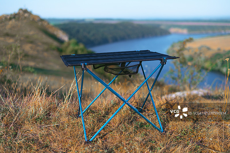 山顶上的小折叠桌，河流背景。自然环境中的旅游装备。配备齐全的假日露营地。无人物。轻便紧凑的装备。图片素材