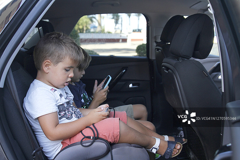 姐弟/兄妹在汽车座位上玩电子游戏图片素材