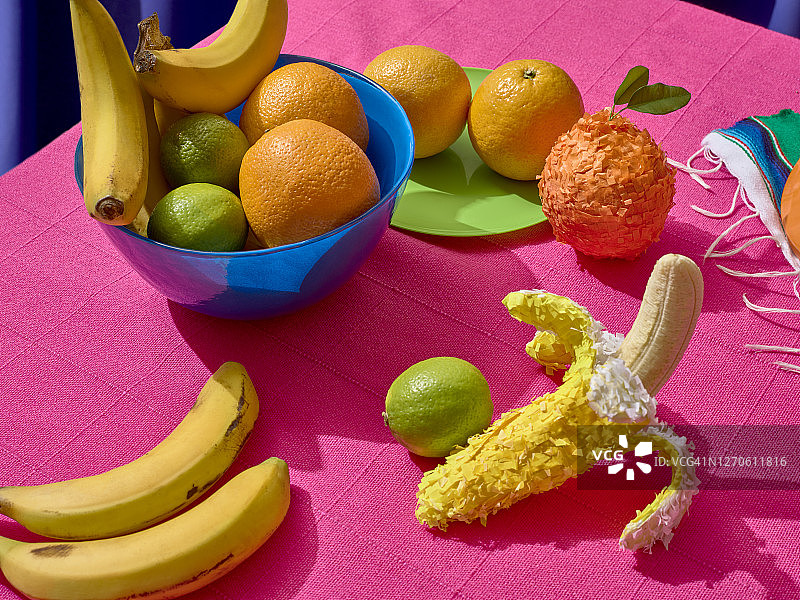 墨西哥盛宴：蓝色碗里的橙子、柠檬和香蕉，粉色背景图片素材