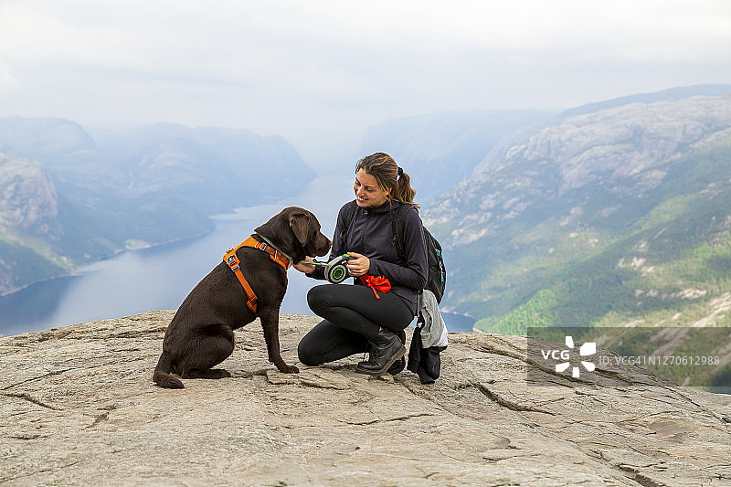 一位女士和她的拉布拉多犬在漫长徒步后欣赏布道石的风景图片素材