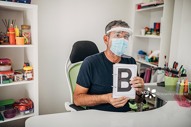 戴着外科口罩和防护面罩的语言治疗师展示字母B图片素材