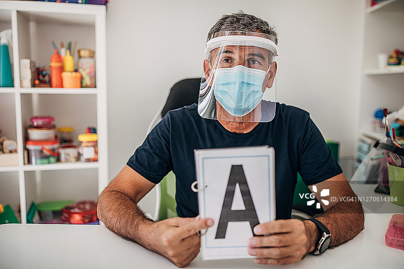 戴外科口罩和防护面罩的言语治疗师展示字母A图片素材