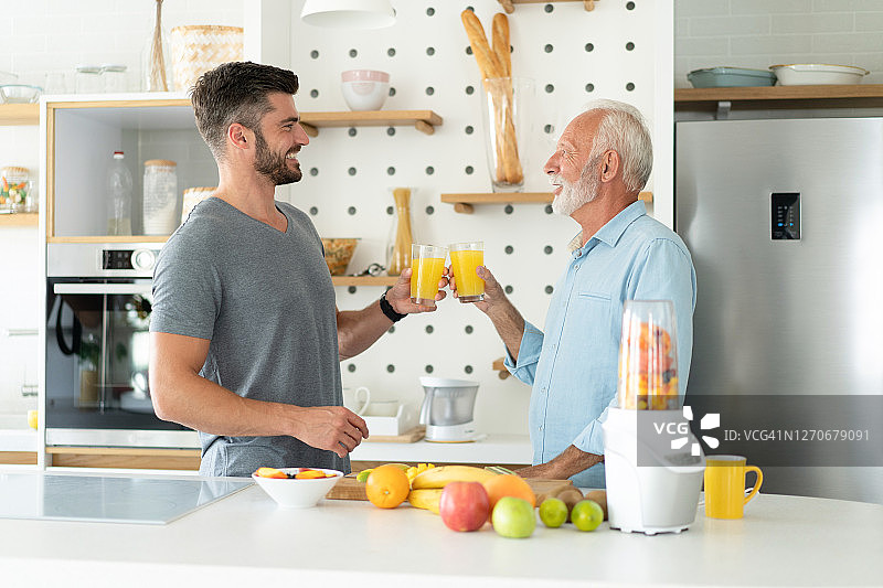 快乐的父子在厨房里喝健康的果汁。图片素材