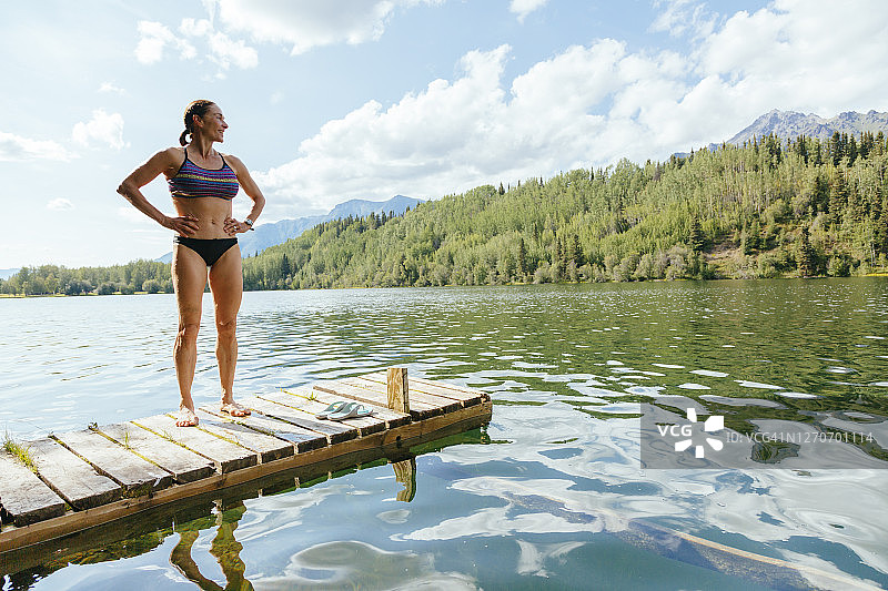 一名女子站在麦卡锡公路沿线的长湖游泳后的码头上，美国阿拉斯加图片素材