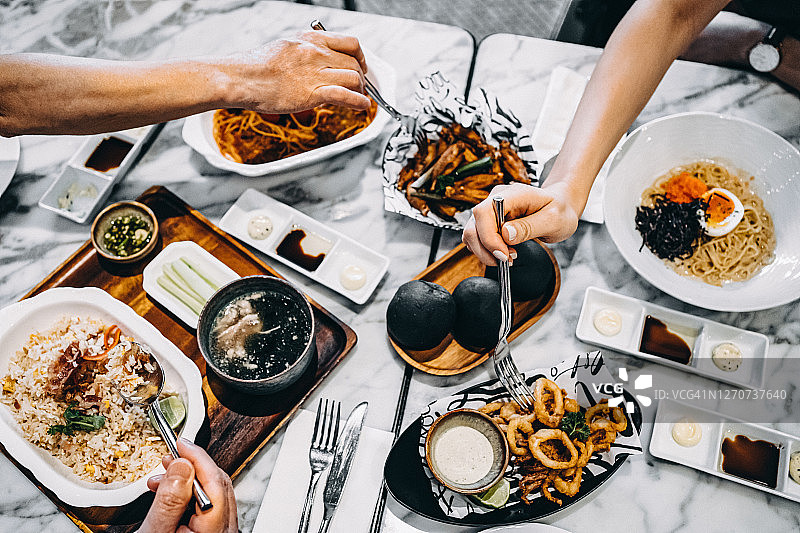 家人/朋友在餐厅用餐，分享各种新鲜菜肴的欢乐时光俯视图图片素材