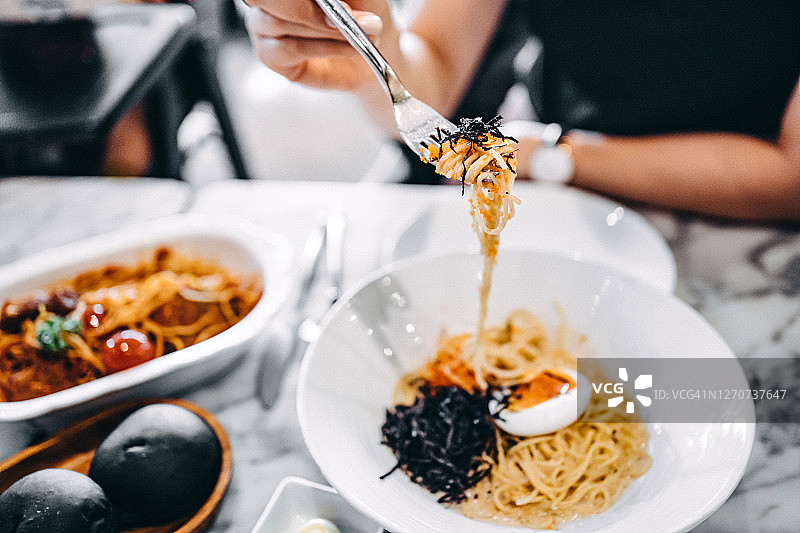 年轻亚洲女性在餐厅享用明太子意面和各种菜肴图片素材