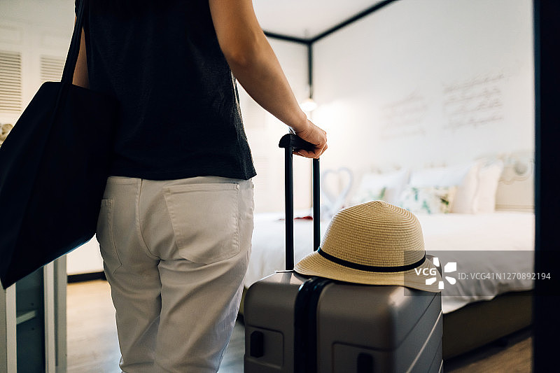亚洲年轻女游客拉着行李箱进入酒店房间的后视图图片素材