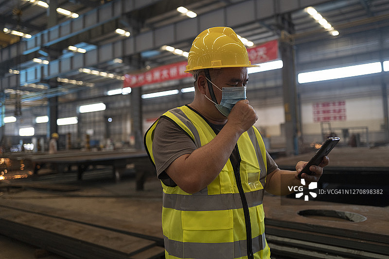 咳嗽的男工程师在车间里使用手机图片素材