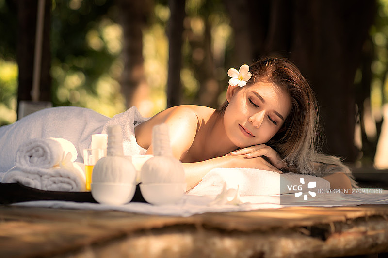 年轻漂亮的亚洲女子在木床上享受按摩和水疗图片素材