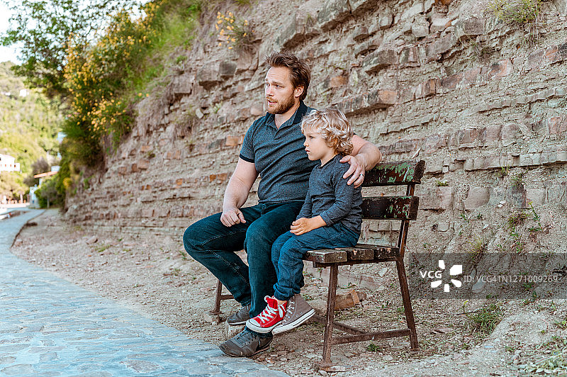 父子坐在户外木制长椅上图片素材
