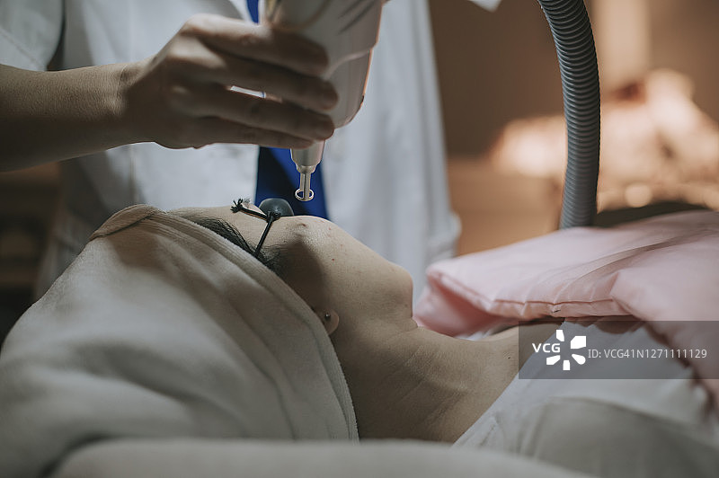 亚洲女性激光脉冲清洁面部皮肤，硬件美容护理，光合作用过程，温暖皮肤，激光碳面部皮肤再生图片素材