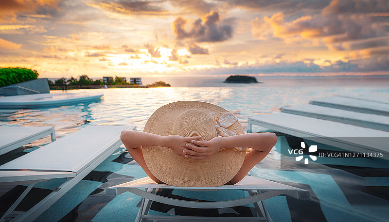 夏日时尚：拥有修长美腿和健康肌肤的比基尼美女戴着太阳帽和太阳镜在游泳池边享受日光浴，享受旅行度假的美好生活图片素材
