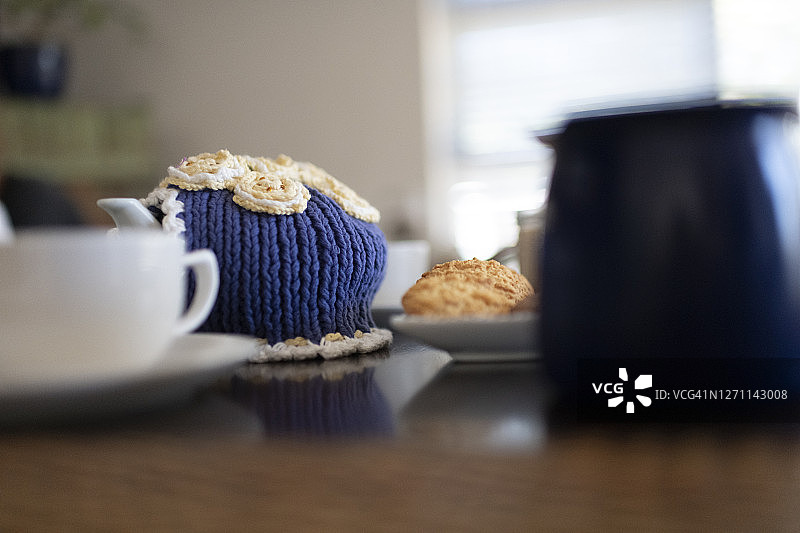 咖啡桌上带针织茶壶罩和饼干的茶壶图片素材