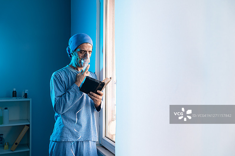 靠窗站立阅读圣经并使用雾化器的成熟男人图片素材