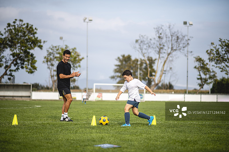 教练观看男孩进行足球运球训练图片素材