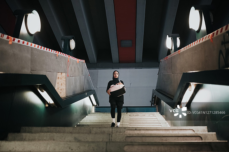 戴着运动头巾的年轻运动女性走下柏林地铁站的混凝土楼梯图片素材