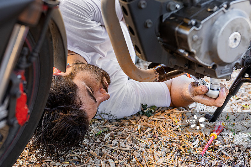 年轻人在摩托车下修理车辆图片素材