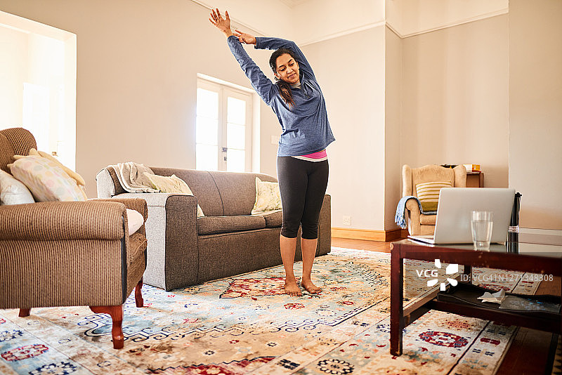 年轻女人在家中上在线瑜伽课时做伸展运动图片素材