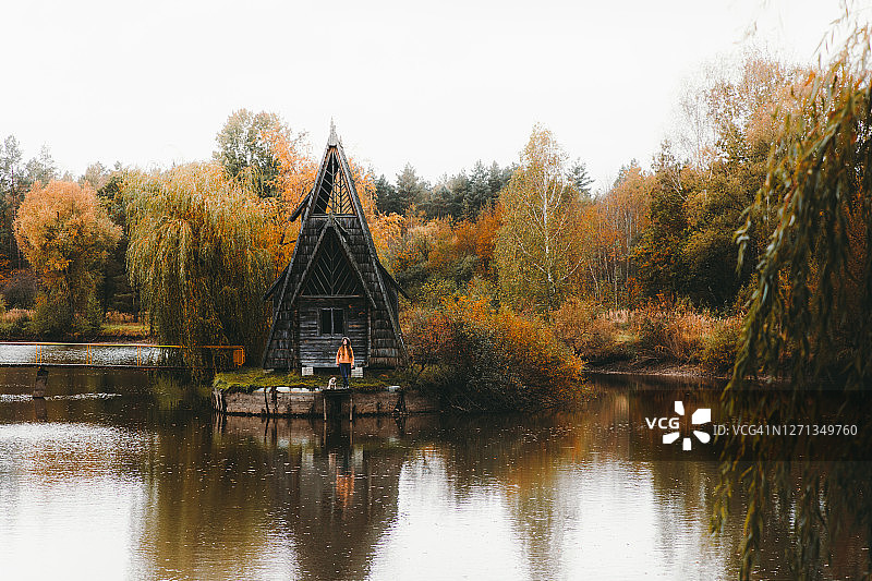 女人和狗在湖边美丽的三角形房子附近迎接明亮的秋天图片素材