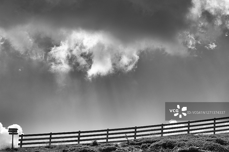 戏剧性天空下的木制栏杆和道路标志剪影图片素材