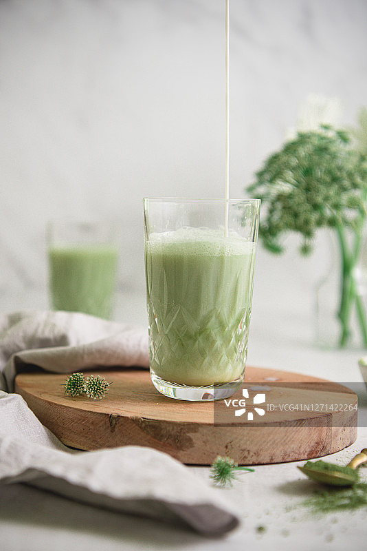 白色桌子上拿铁杯中倒入牛奶的冰镇抹茶特写图片素材