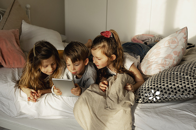 孩子们在床上使用平板电脑图片素材