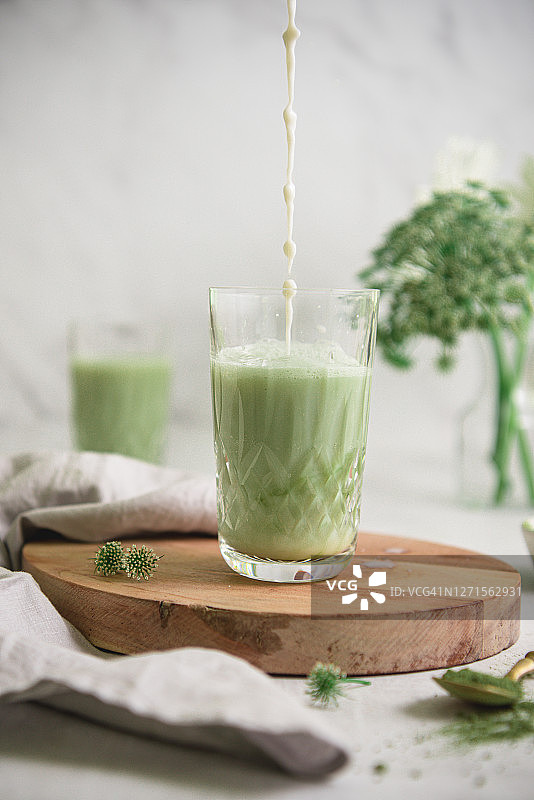 白色桌子上拿铁杯中倒入牛奶的冰镇抹茶特写图片素材