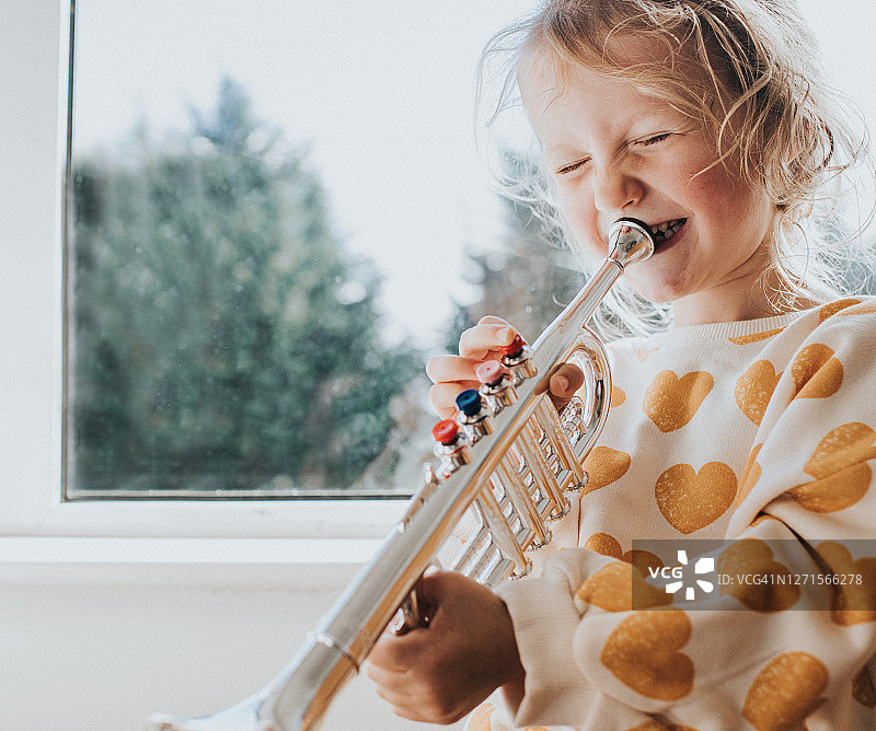 小女孩用力吹着玩具喇叭，咯咯地笑着图片素材
