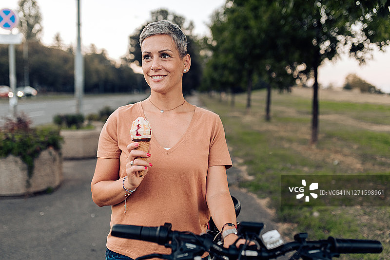 快乐的女人吃冰淇淋并推着自行车的肖像图片素材